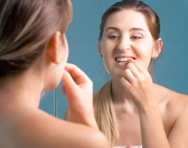 Young woman cleaning and checking her teeth at mirror in bathroom.